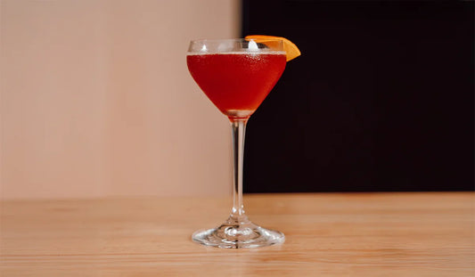 Paper Plane cocktail with an orange peel sitting on a table